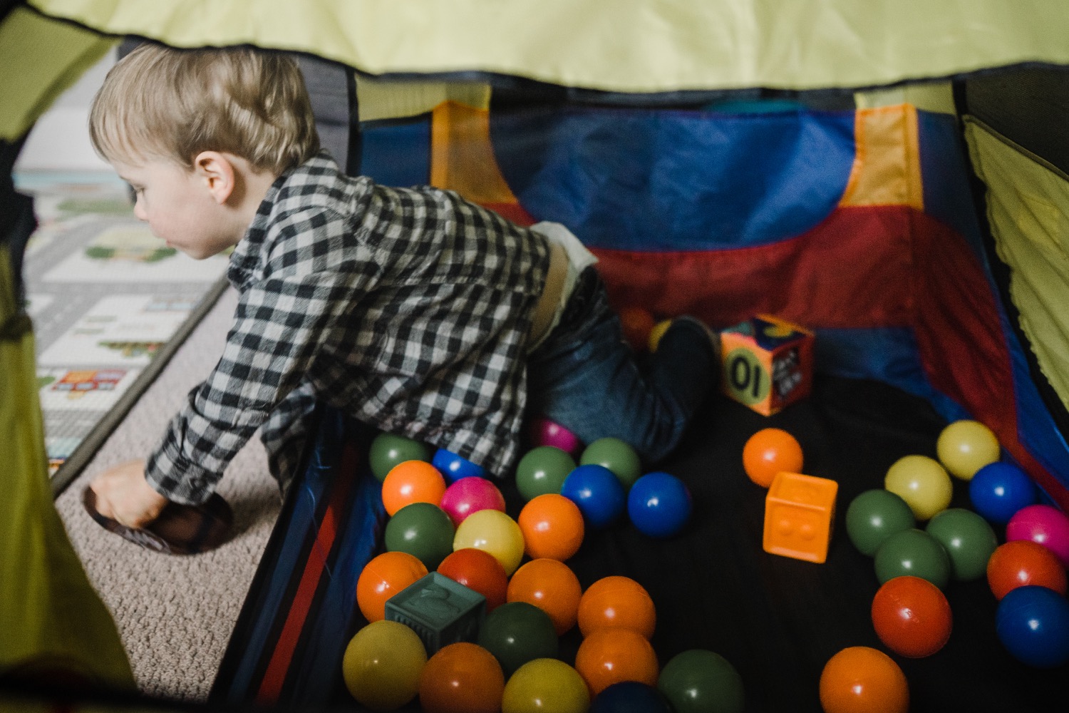Little boy in plaid shirt crawling out of ball pit