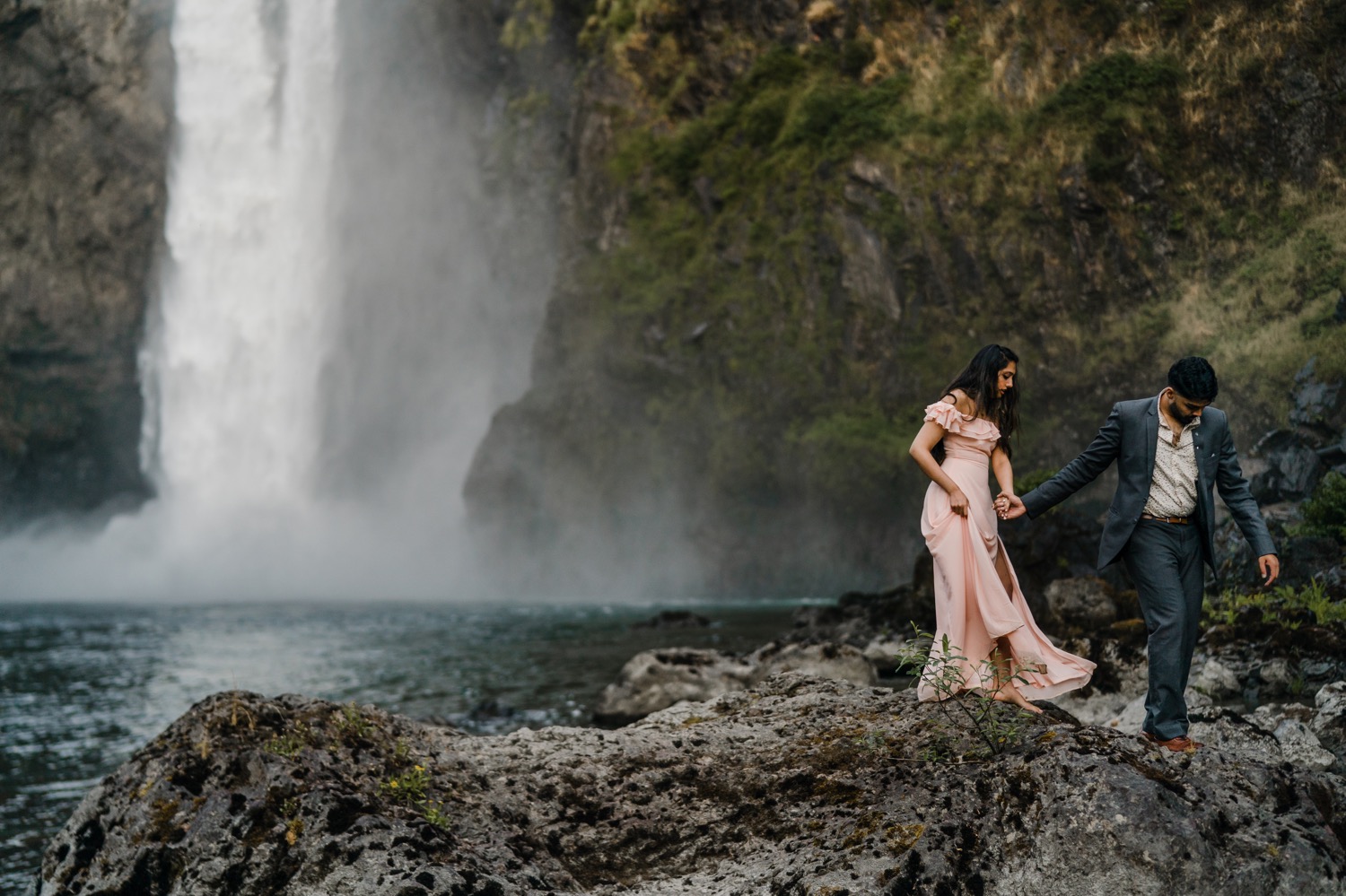 Couple holding hands walking off rocks in front of Snoqualmie Falls