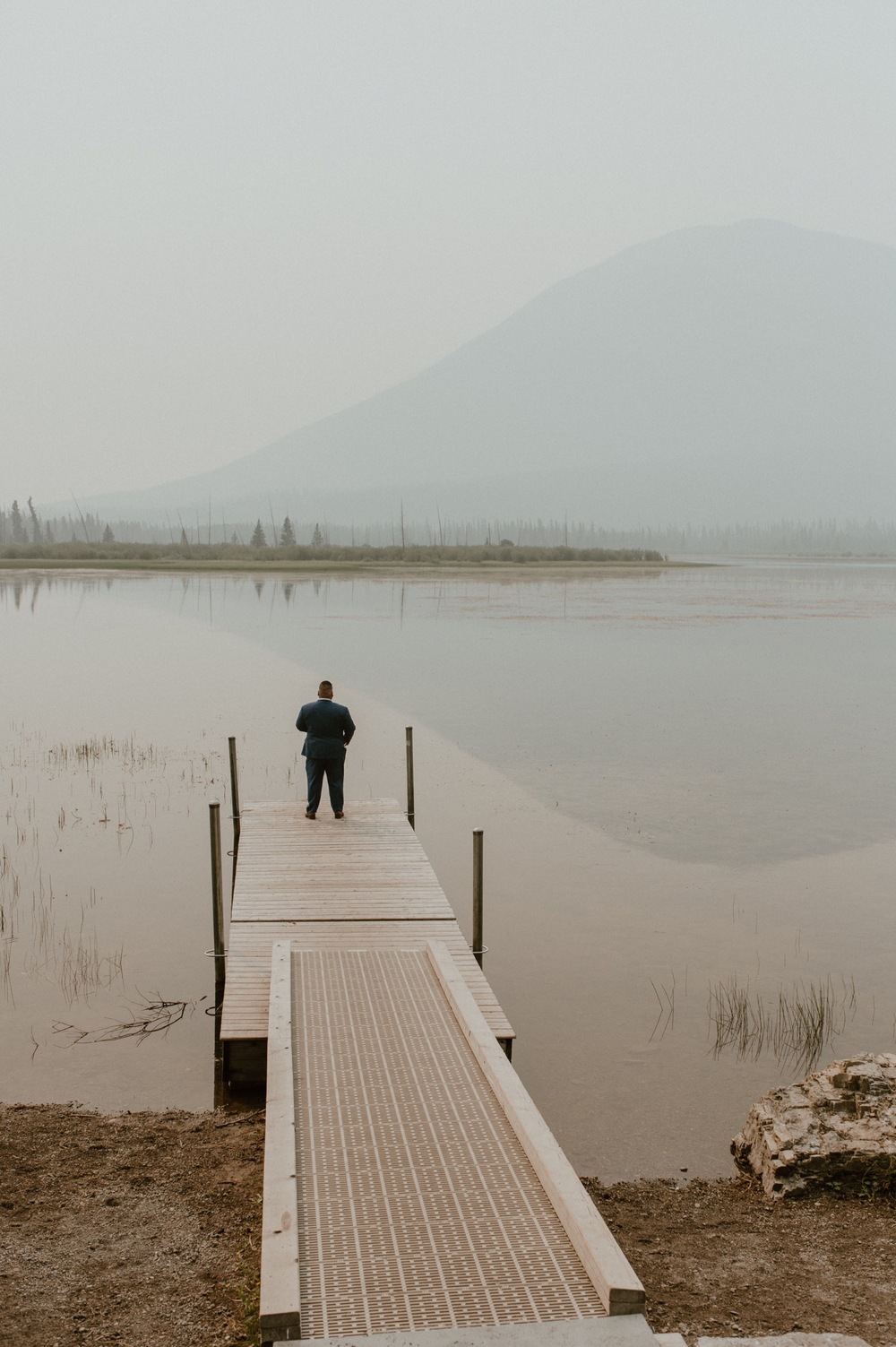 groom standing on a dock waiting to do his first look with his bride for a mountain elopement during wildfire season in Banff Alberta