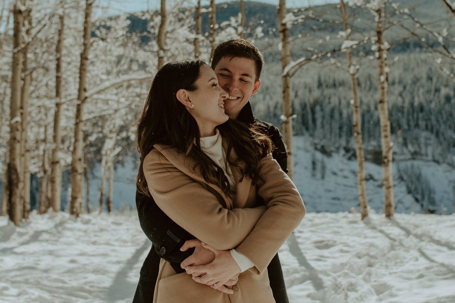 couple embracing each other in a forest during a winter engagement session in the rocky mountains of alberta