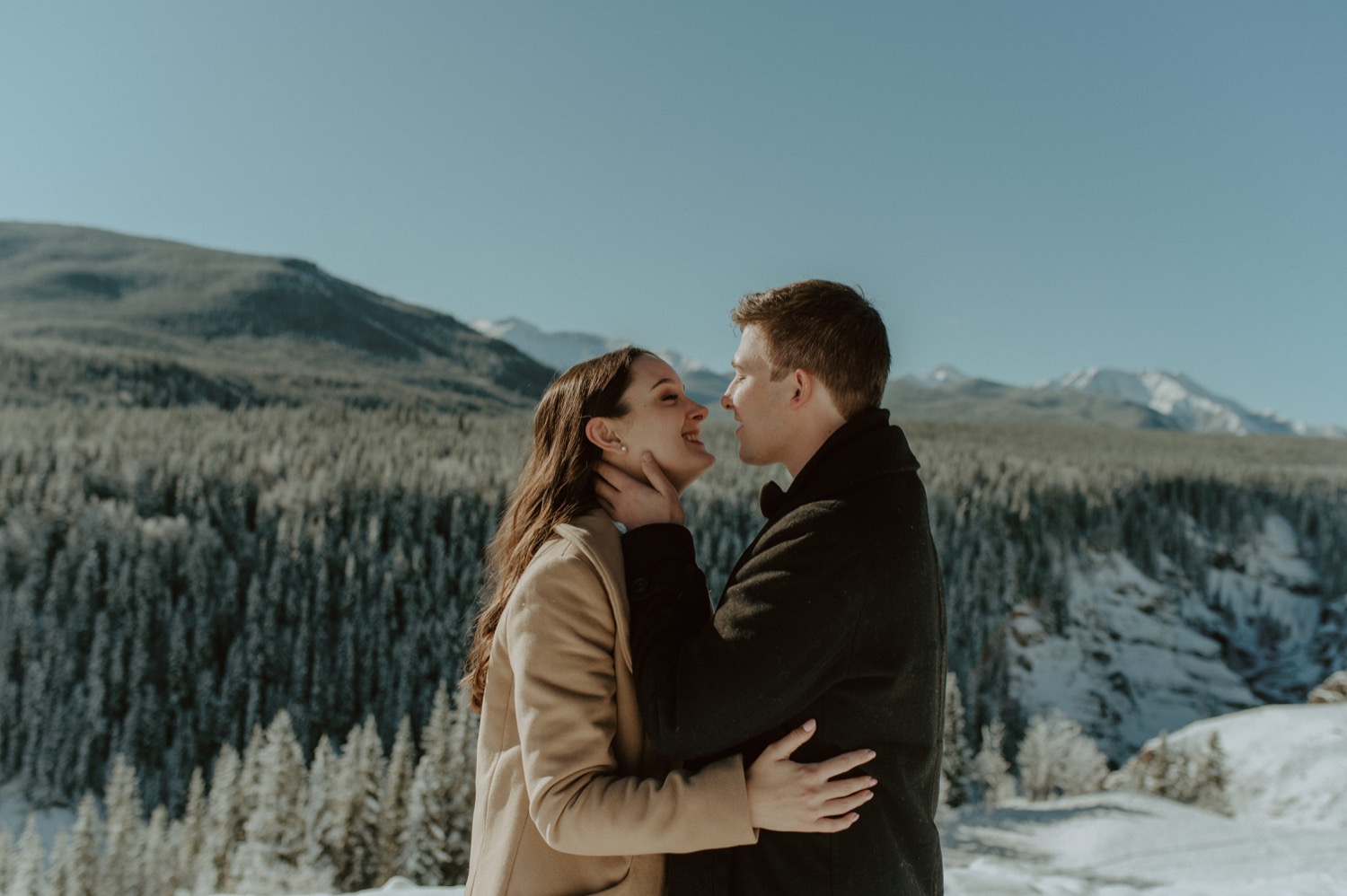 couple embracing each other in front of a winter mountain back drop for their engagement session in Alberta