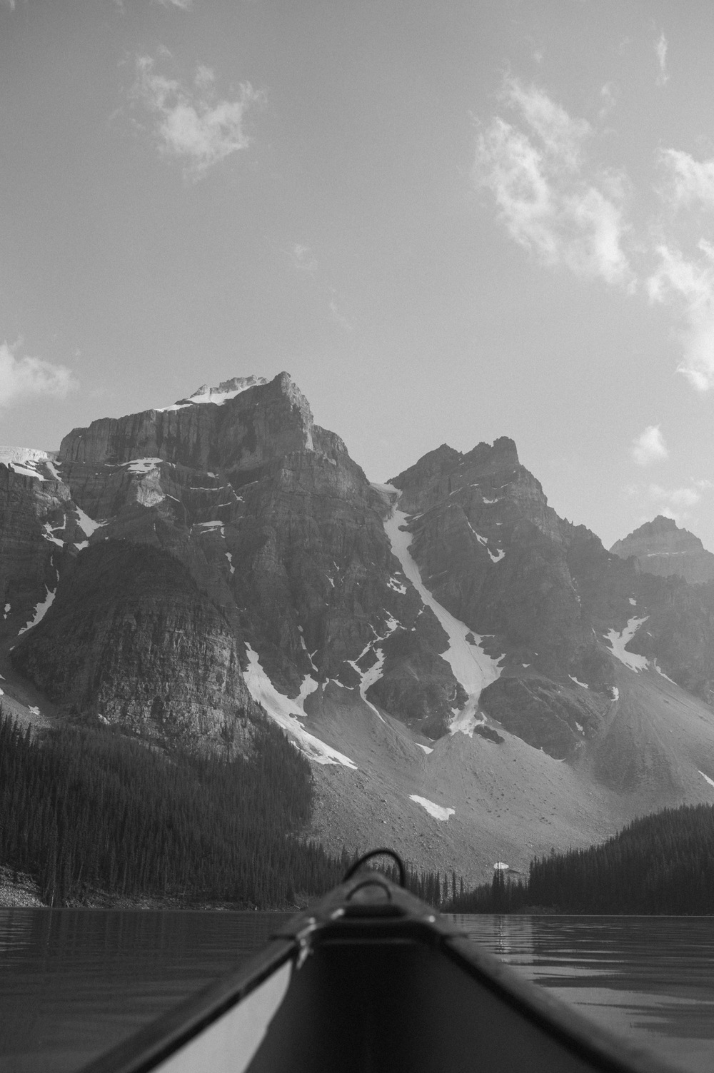 black and white shot of mountain peaks surrounding Moraine Lake from a canoe in the summer
