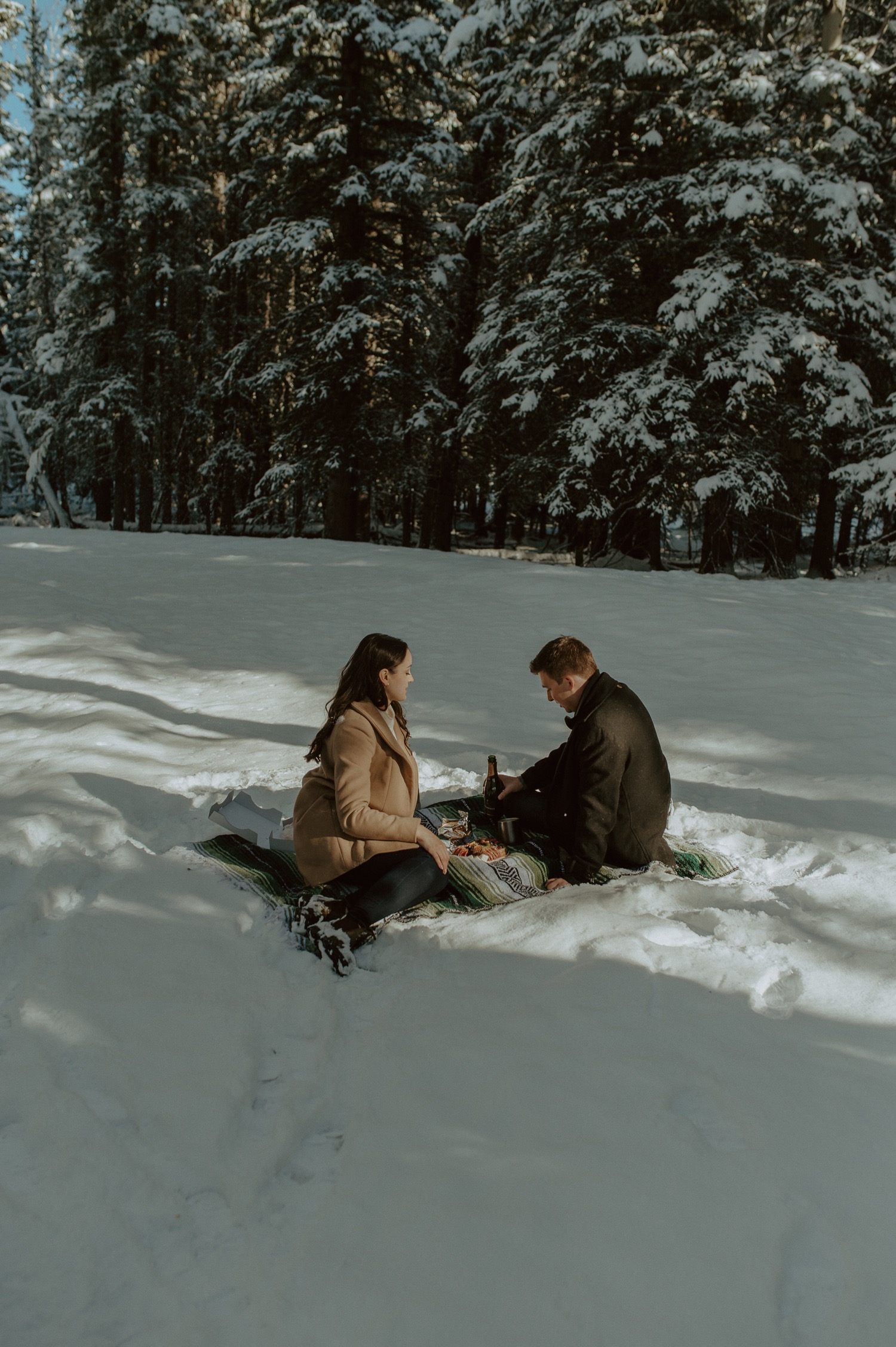 couple sitting in the snow for a winter picnic during a winter engagement session in the rocky mountains of alberta