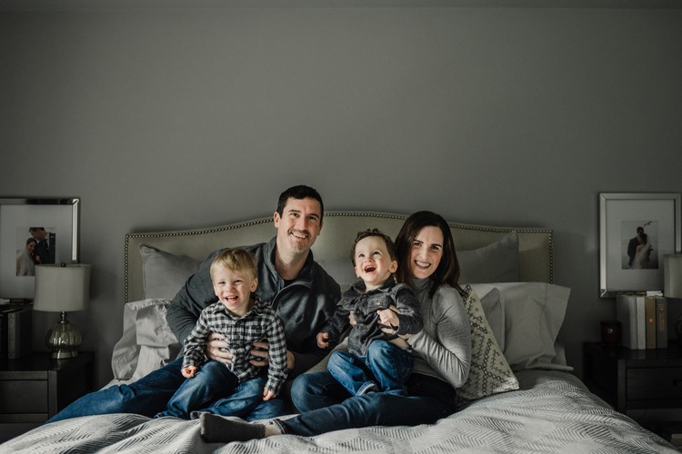 Family of 4 sitting on bed smiling for the camera
