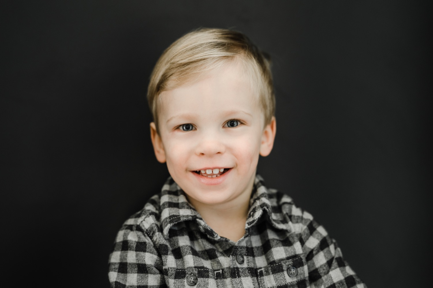 Little boy in plaid shirt sitting and smiling at the camera