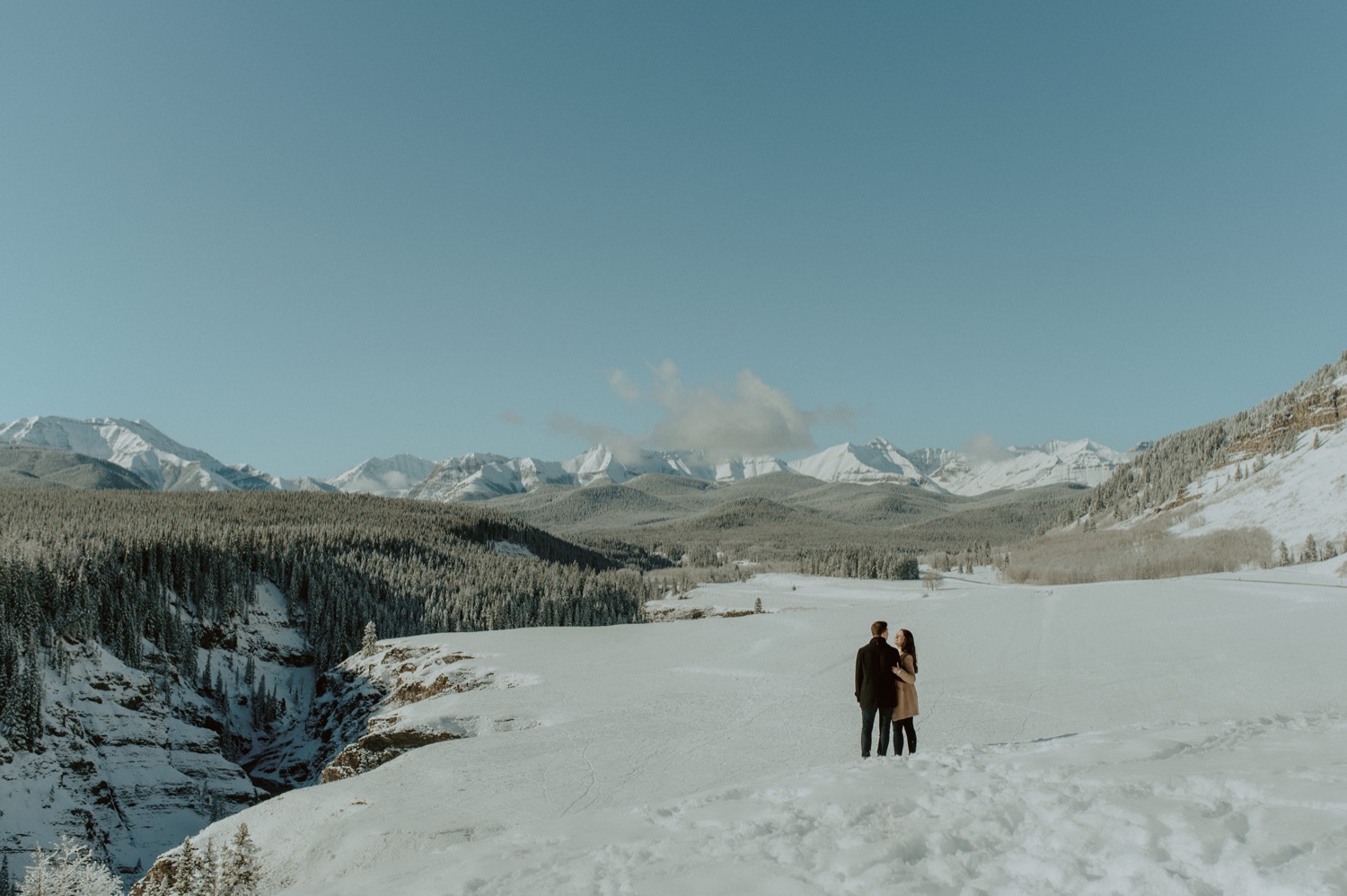 big landscape shot of couple looking out at amazing mountain backdrop during a winter engagement session in the rocky mountains of Alberta