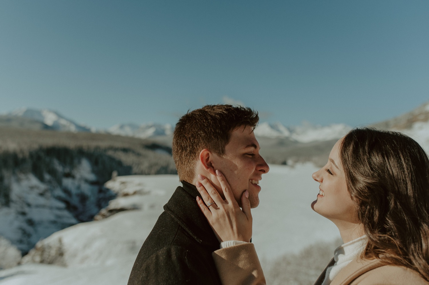 candid shot of couple holding each other in front of amazing mountain backdrop during a winter engagement session in the rocky mountains of Alberta