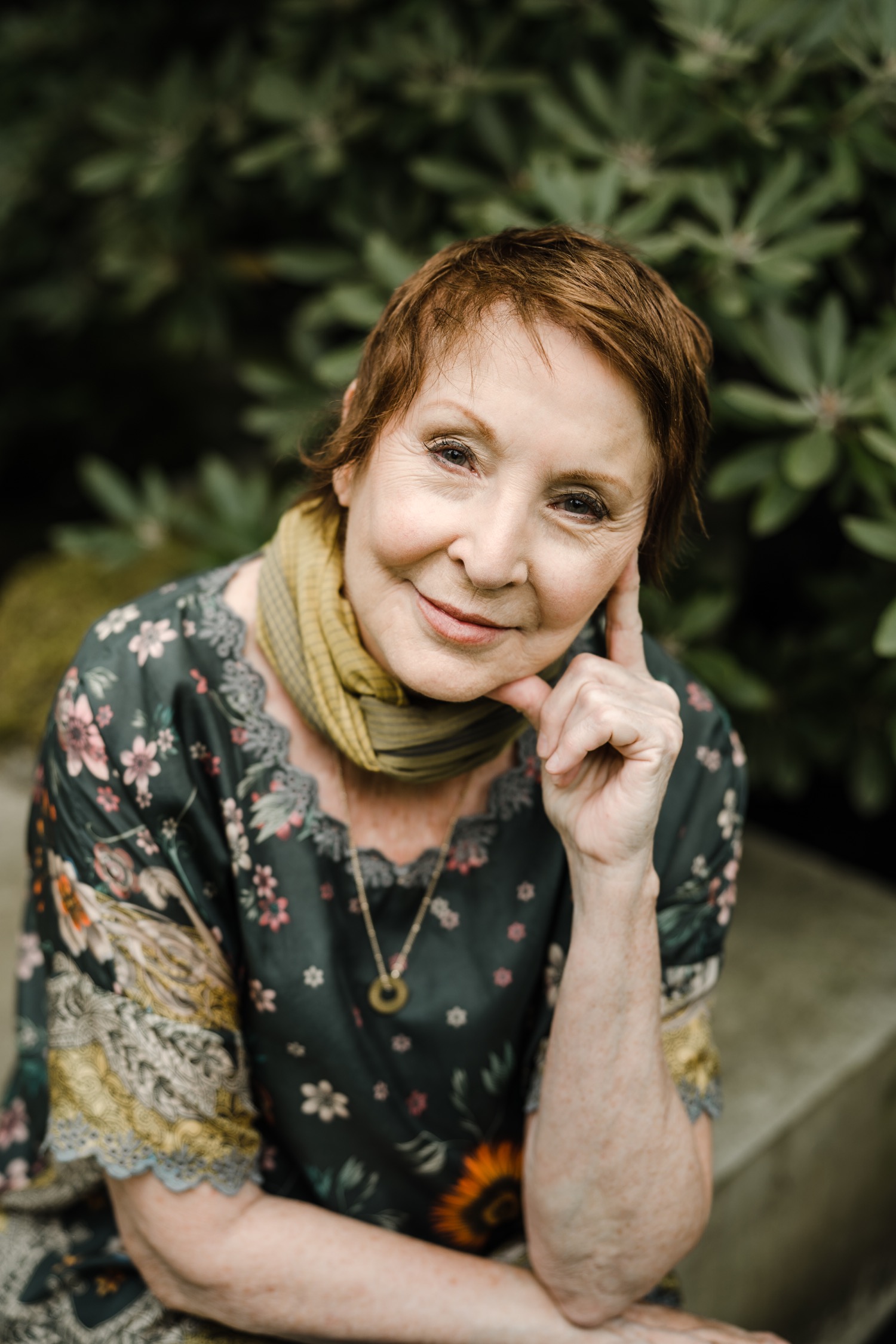 Woman in green floral blouse resting head on hand smiling at the camera for female author portraits