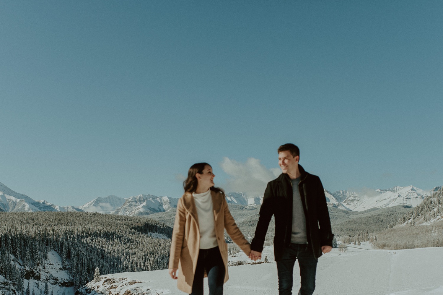 couple walking in front of amazing mountain backdrop during a winter engagement session in the rocky mountains of Alberta