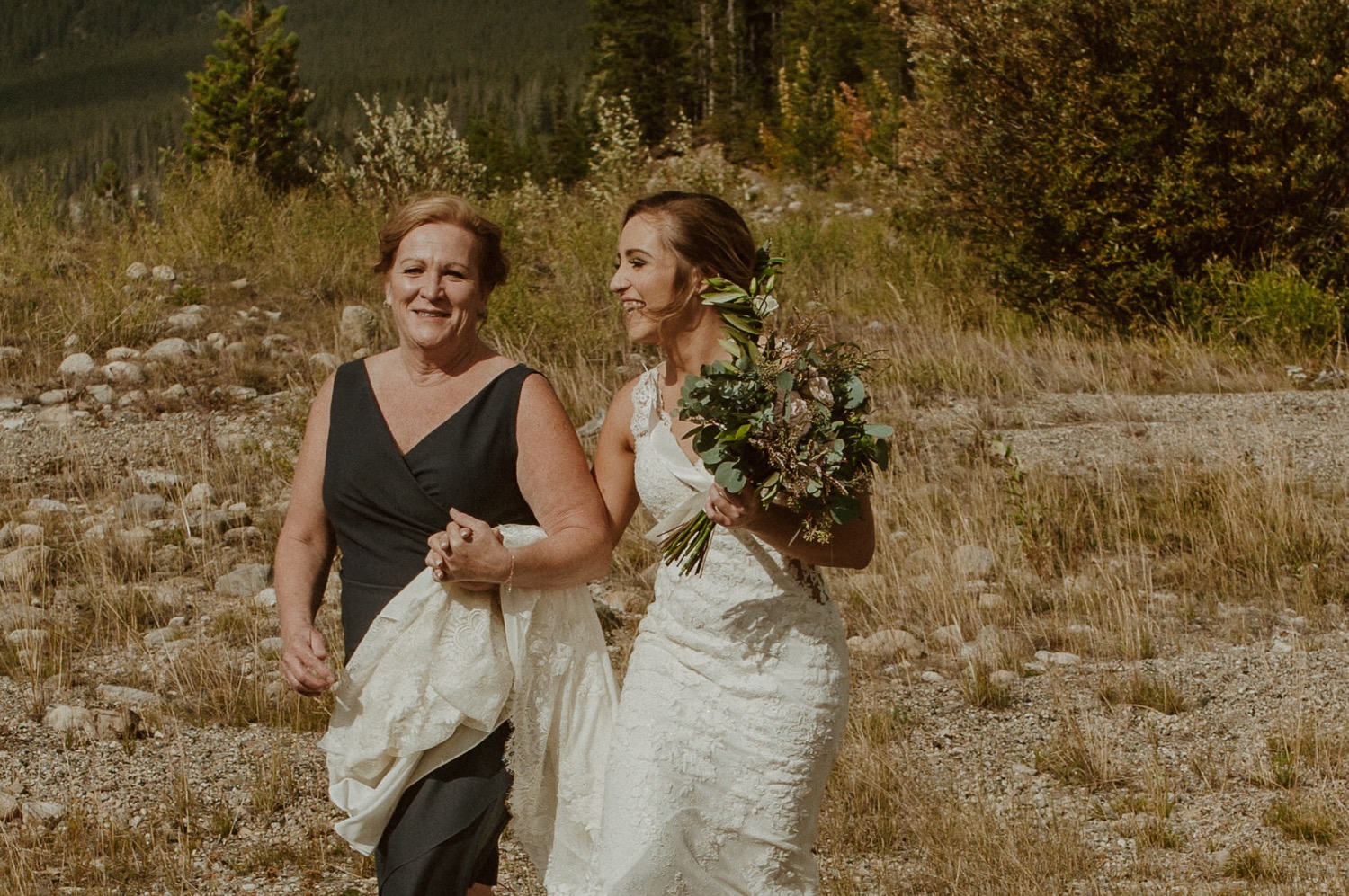 The mother walks the bride down the make shift aisle for their ceremony on the shore of Spray Lakes Alberta
