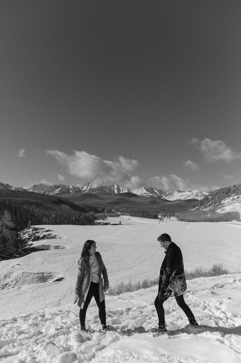 black and white shot of couple having fun in the snow with amazing backdrop during a winter engagement session in Kananaskis Alberta
