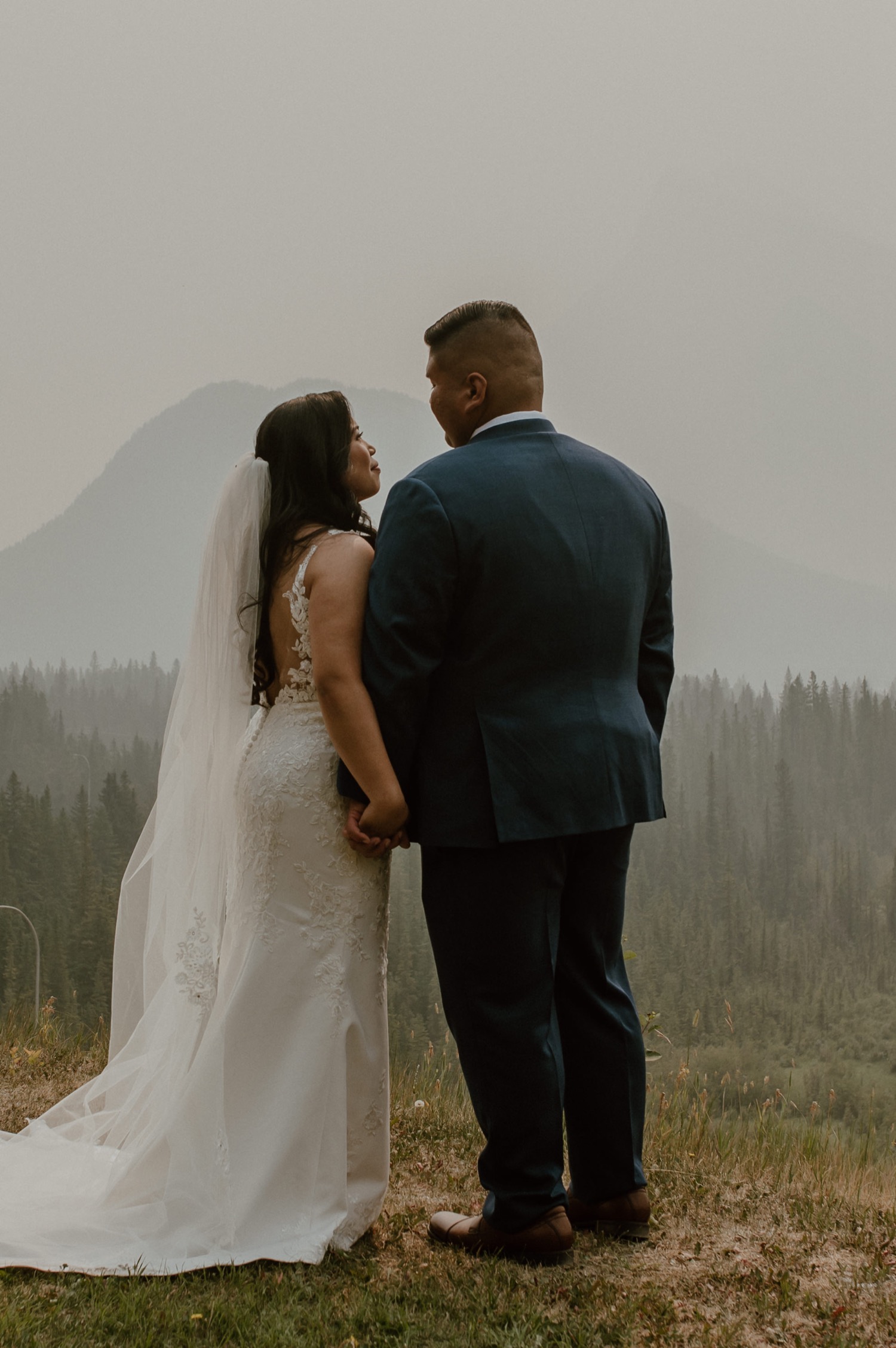 bride and groom standing looking out at the view outside of their hotel for a mountain elopement during wildfire season in Banff Alberta
