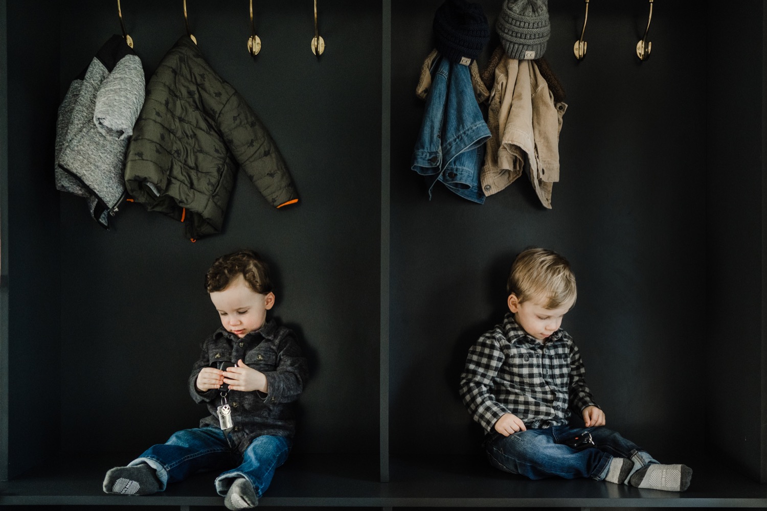 Twin baby boys sitting in coat cubbies playing with keys