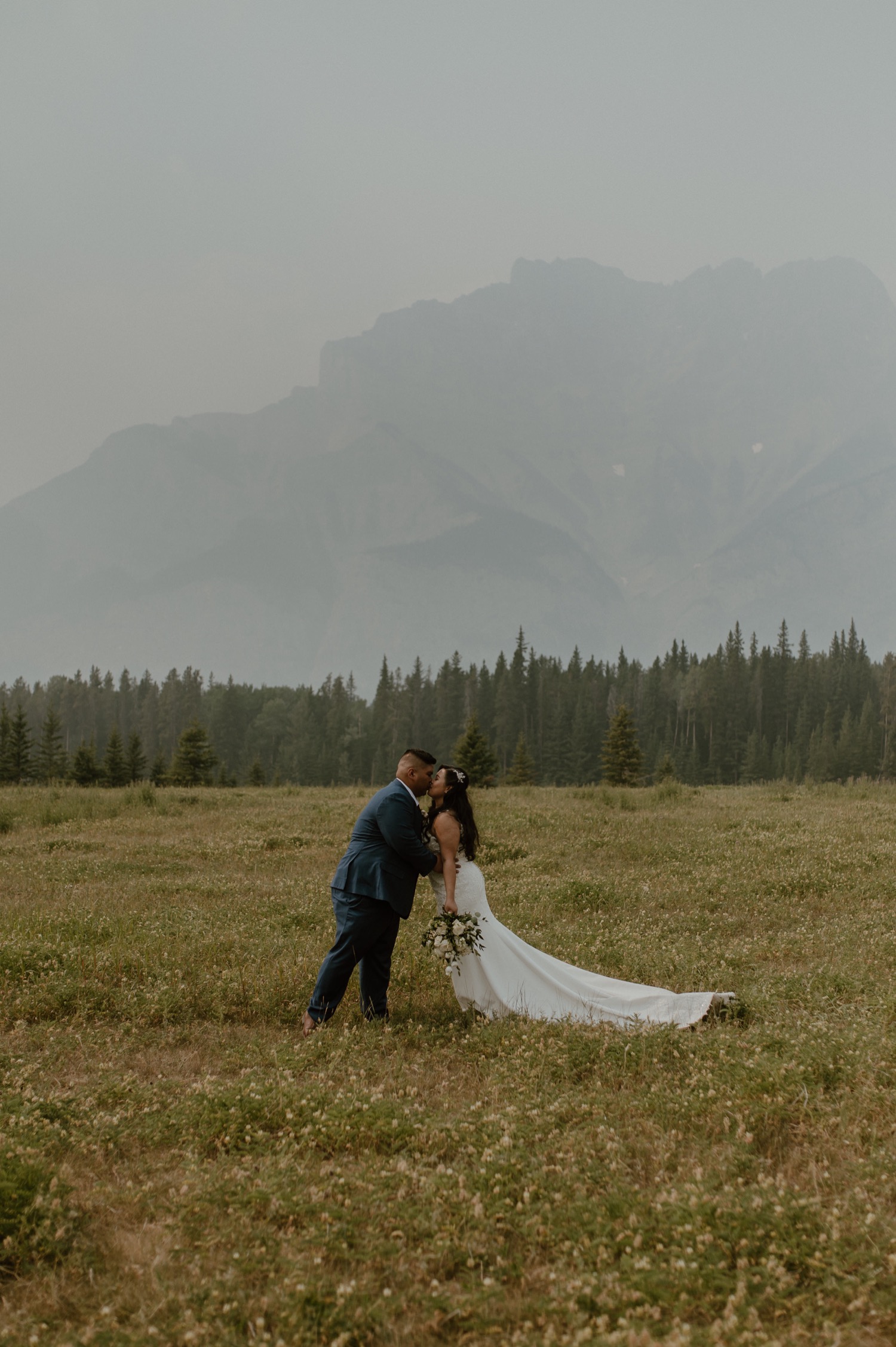 bride and groom kissing in big landscape shot for a mountain elopement during wildfire season in Banff Alberta