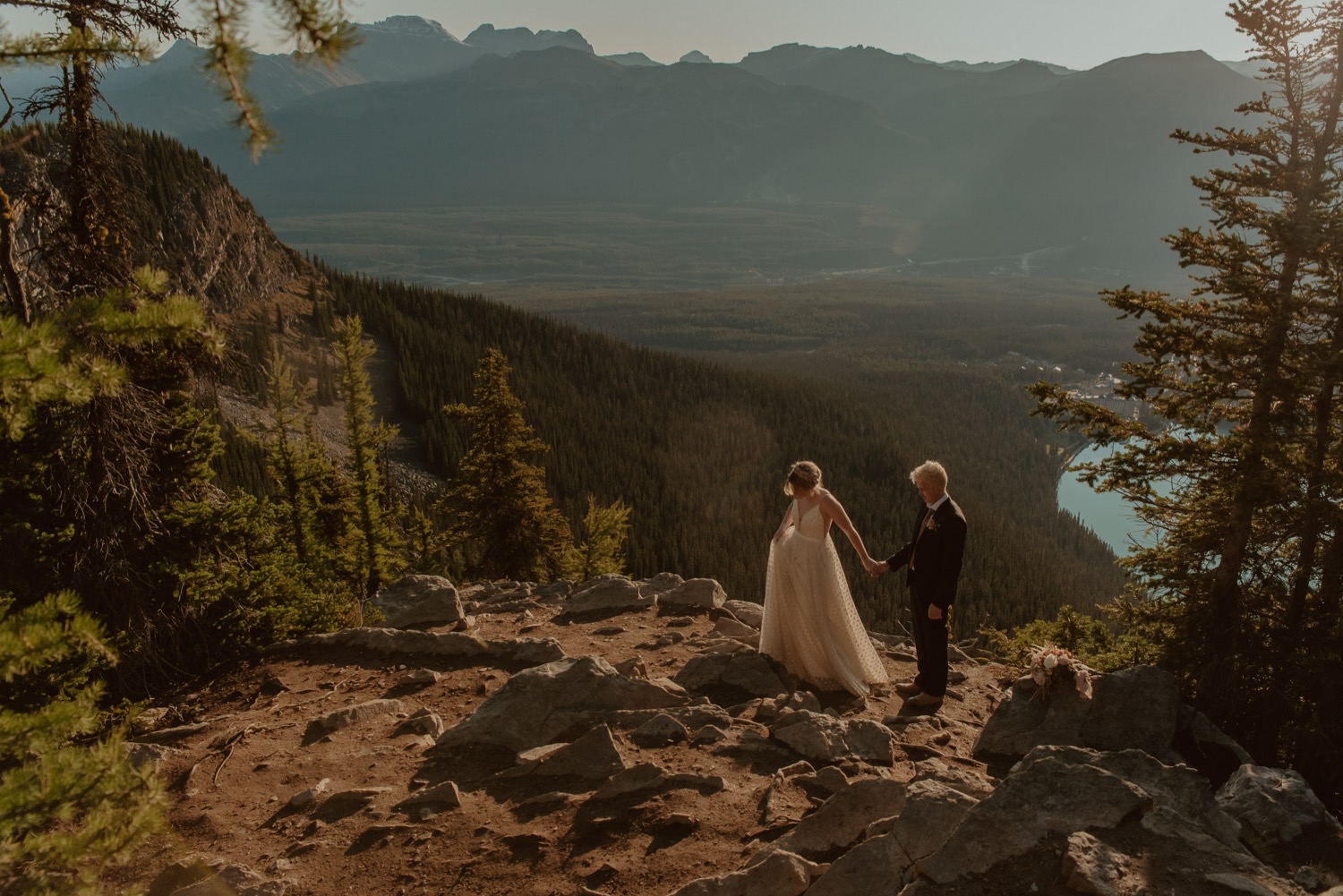 bride leading groom across mountain trail above Lake Louise Alberta during a hiking sunrise elopement