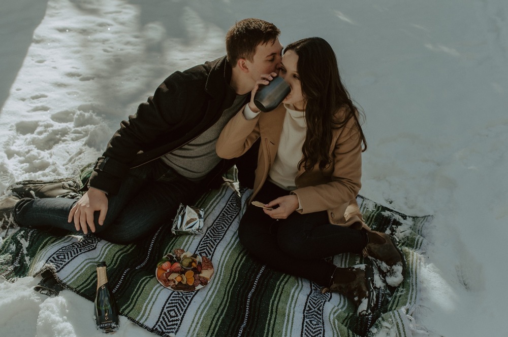 candid shot of couple enjoying a winter picnic during a winter engagement session in the rocky mountains of Alberta
