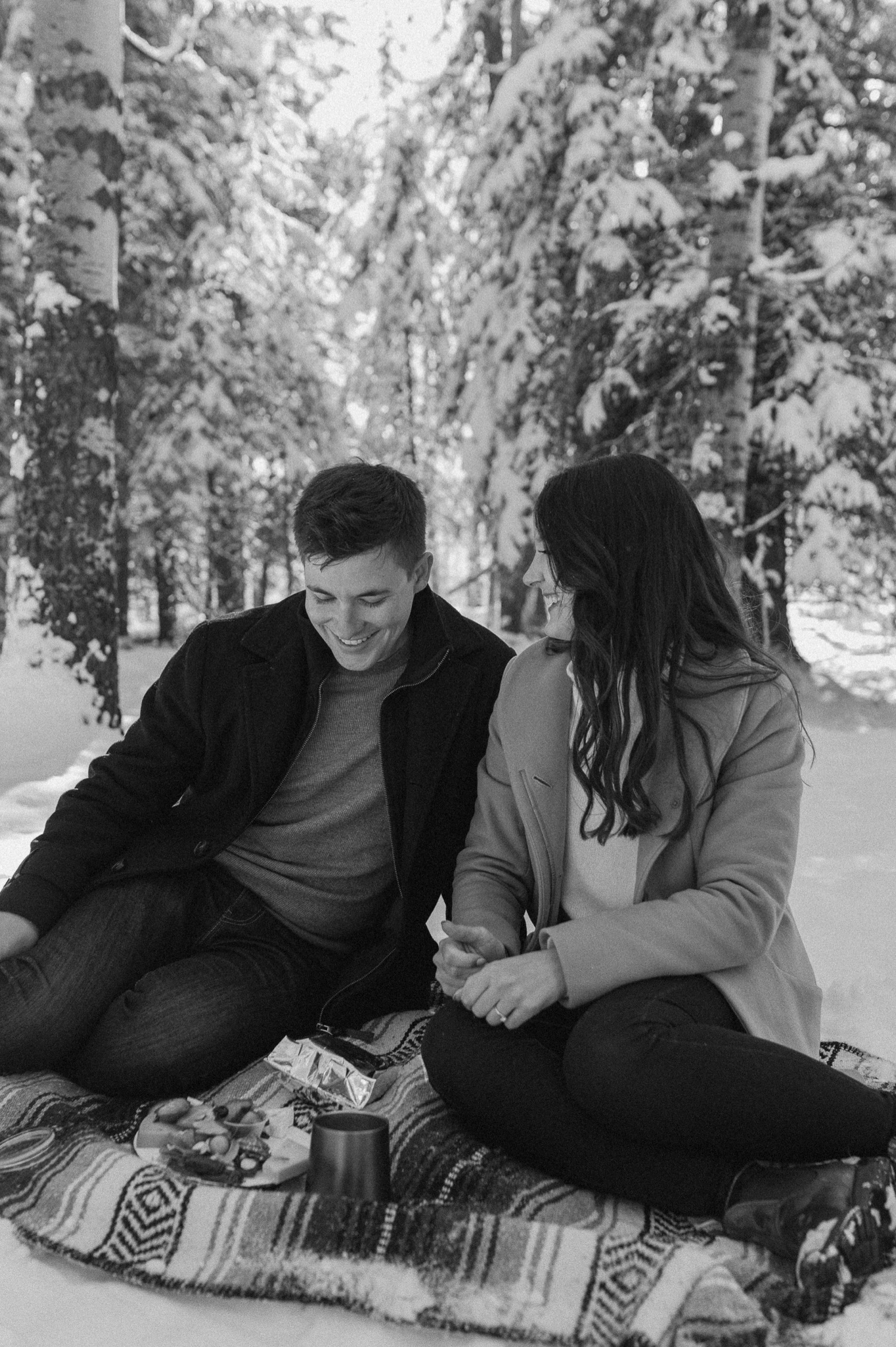 black and white candid photo of couple enjoying a winter picnic during a winter engagement session in the rocky mountains of Alberta