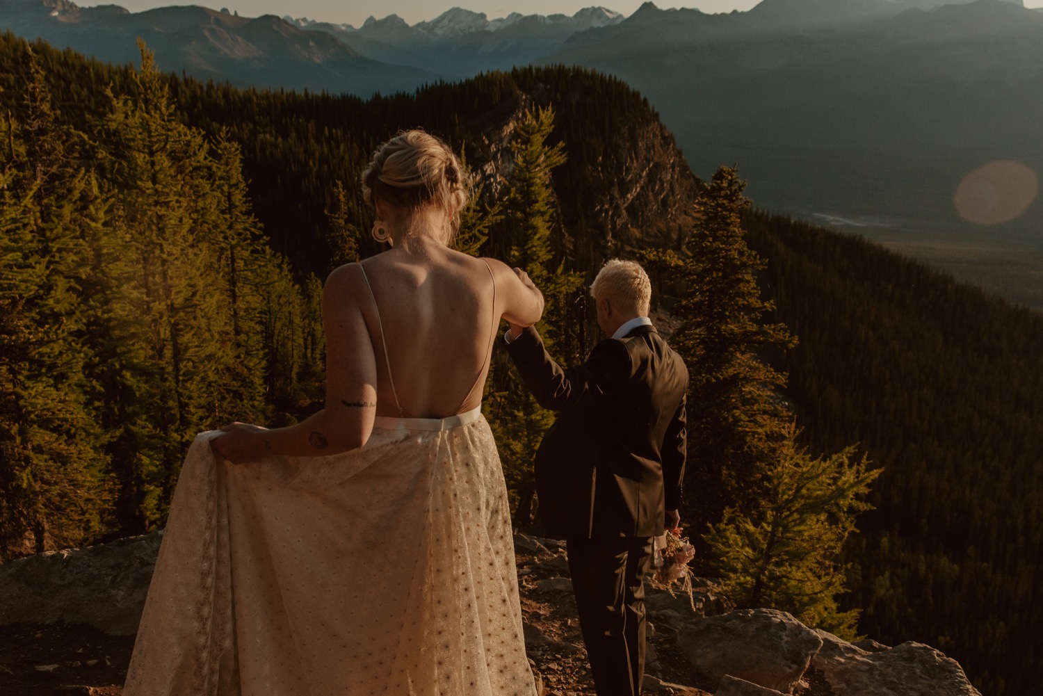 groom leading bride down trail during sunrise on top of a mountain for a hiking style elopement in Lake Louise Alberta