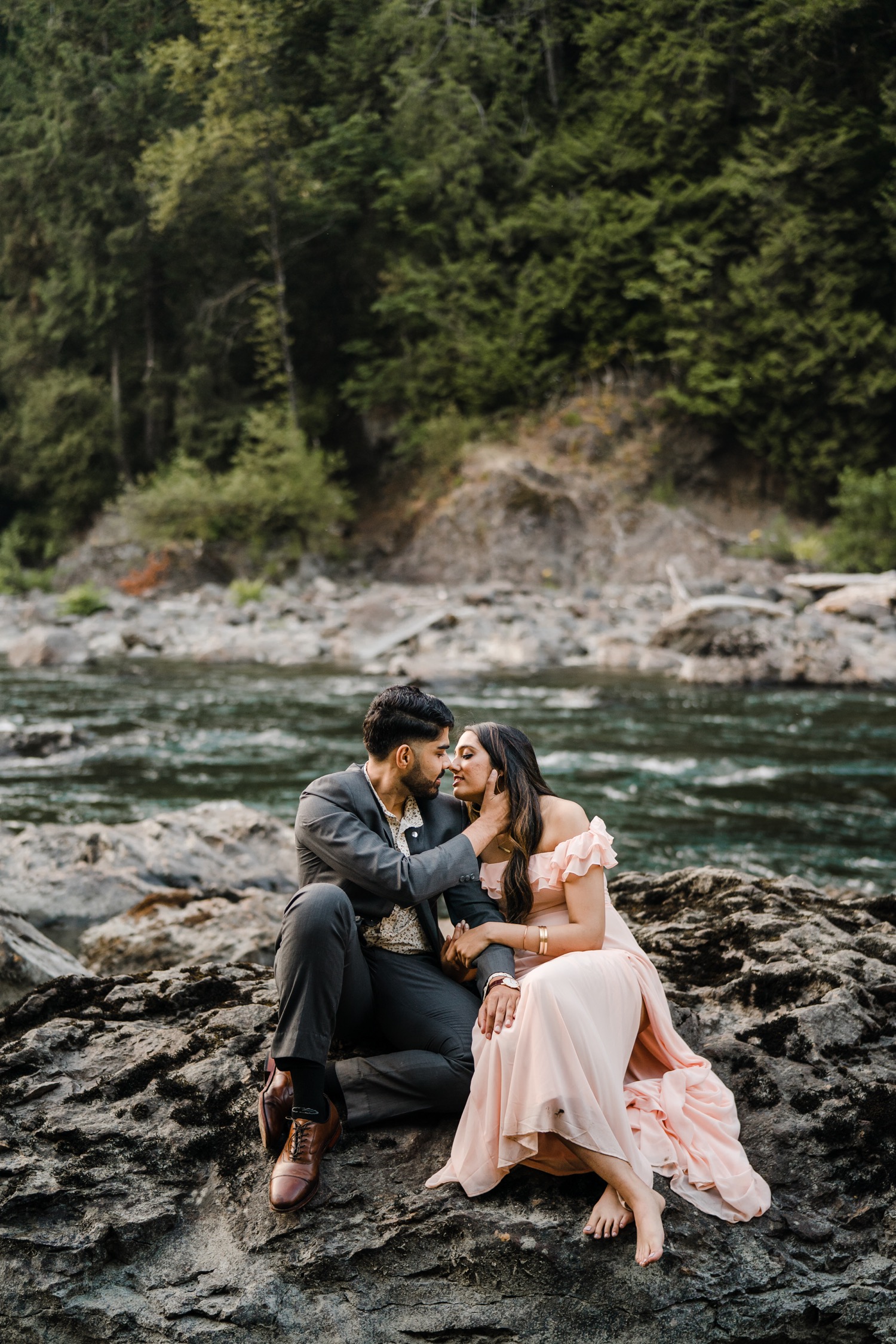 Couple leaning in for a kiss while sitting on rocks in the river.