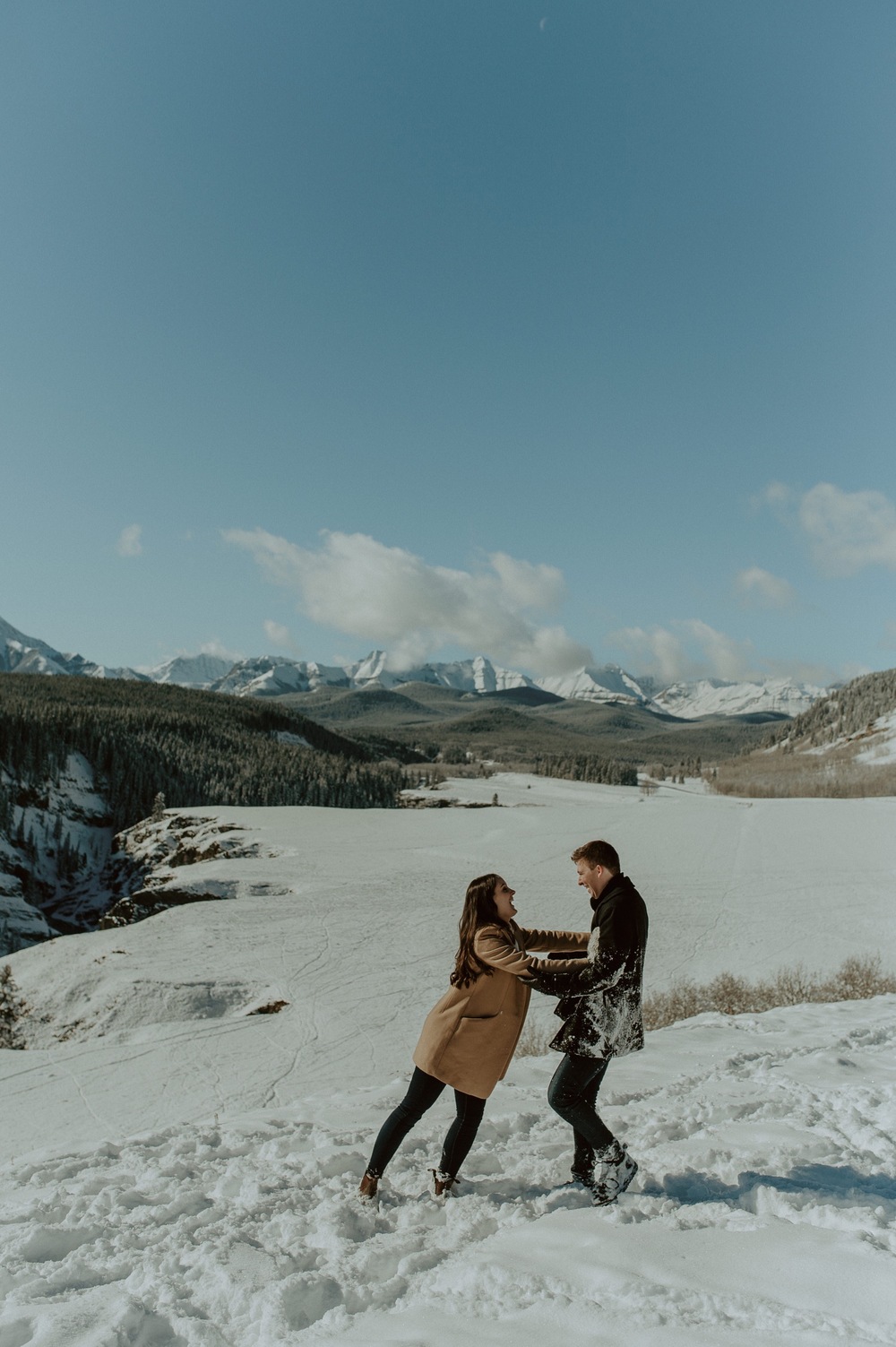 candid shot of couple having fun in the snow in front of amazing back drop in Kananaskis Alberta