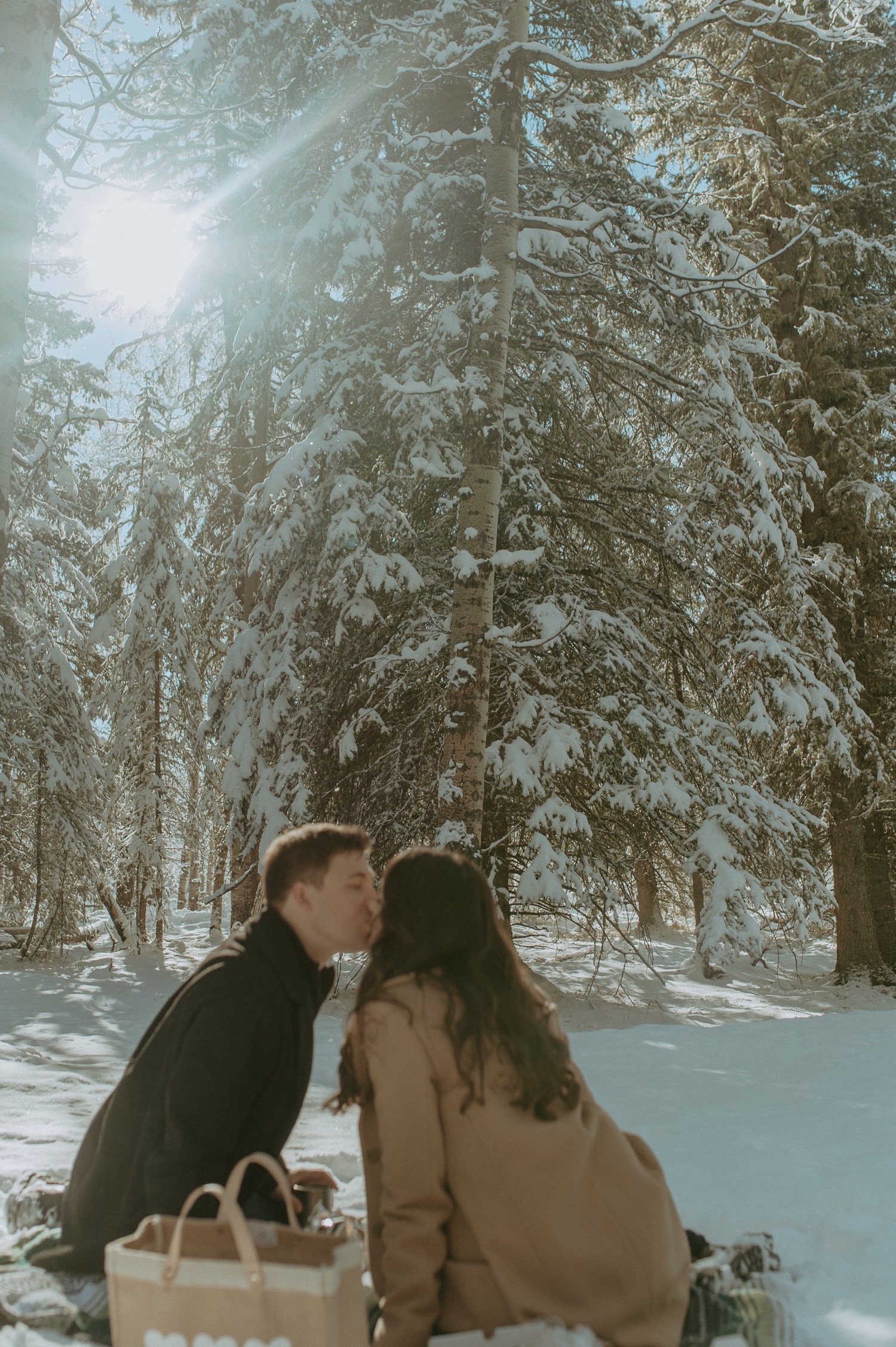 out of focus shot with sun flare of couple enjoying a winter picnic during a winter engagement session in the rocky mountains of Alberta