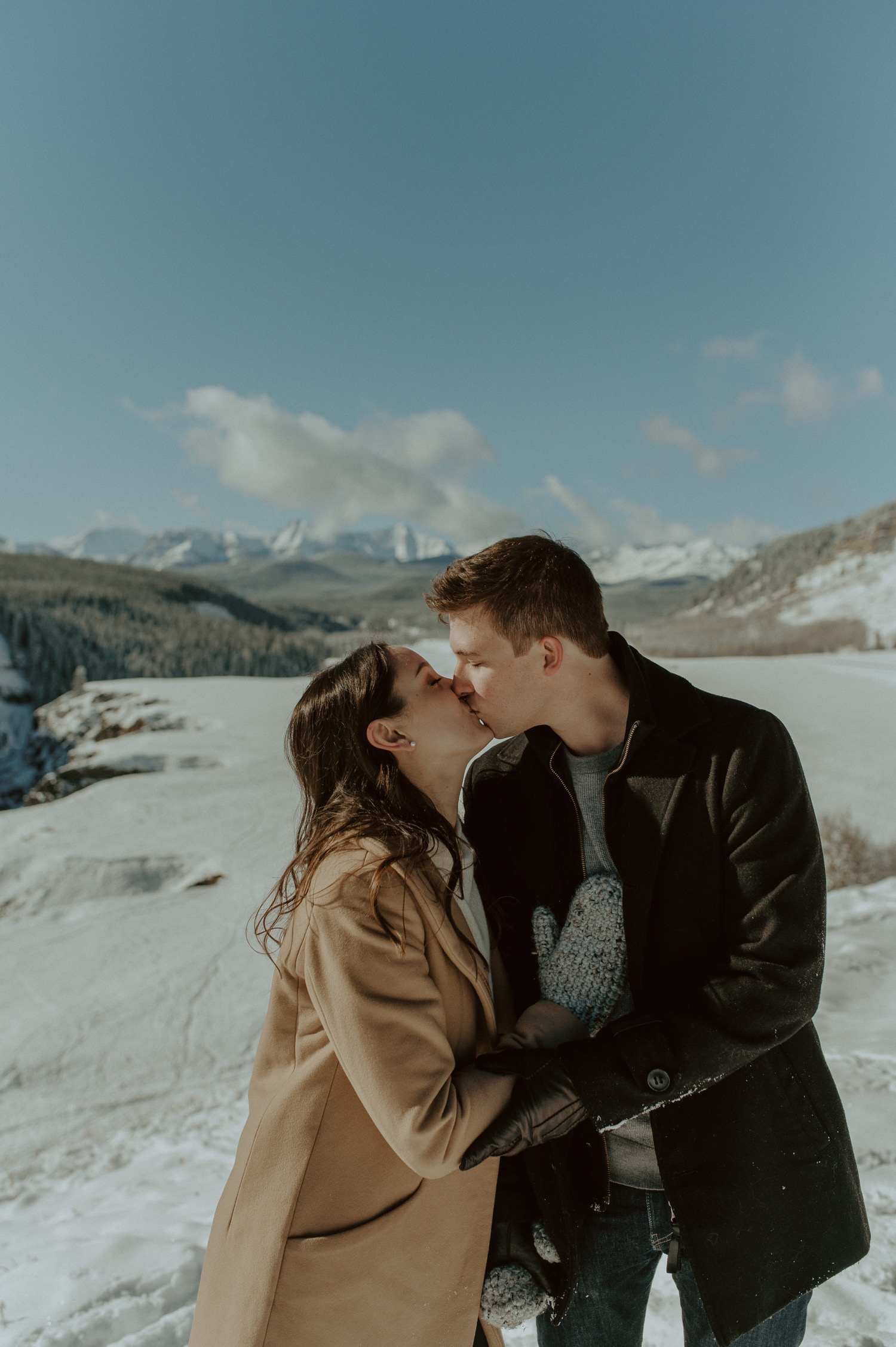 couple kissing in front of winter mountain back drop for an engagement session in Kananasks Alberta