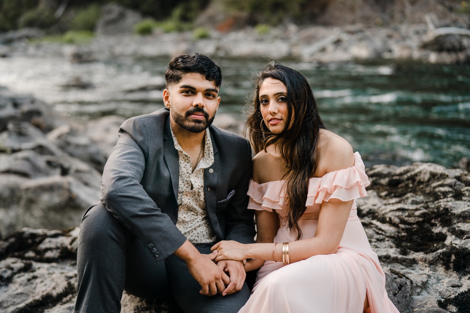 Couple sitting on rocks by the river looking into the camera