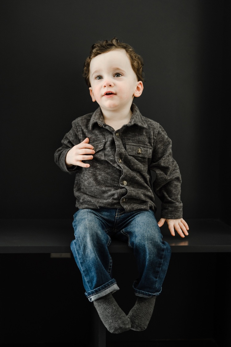Little boy in gray shirt sitting and smiling at the camera