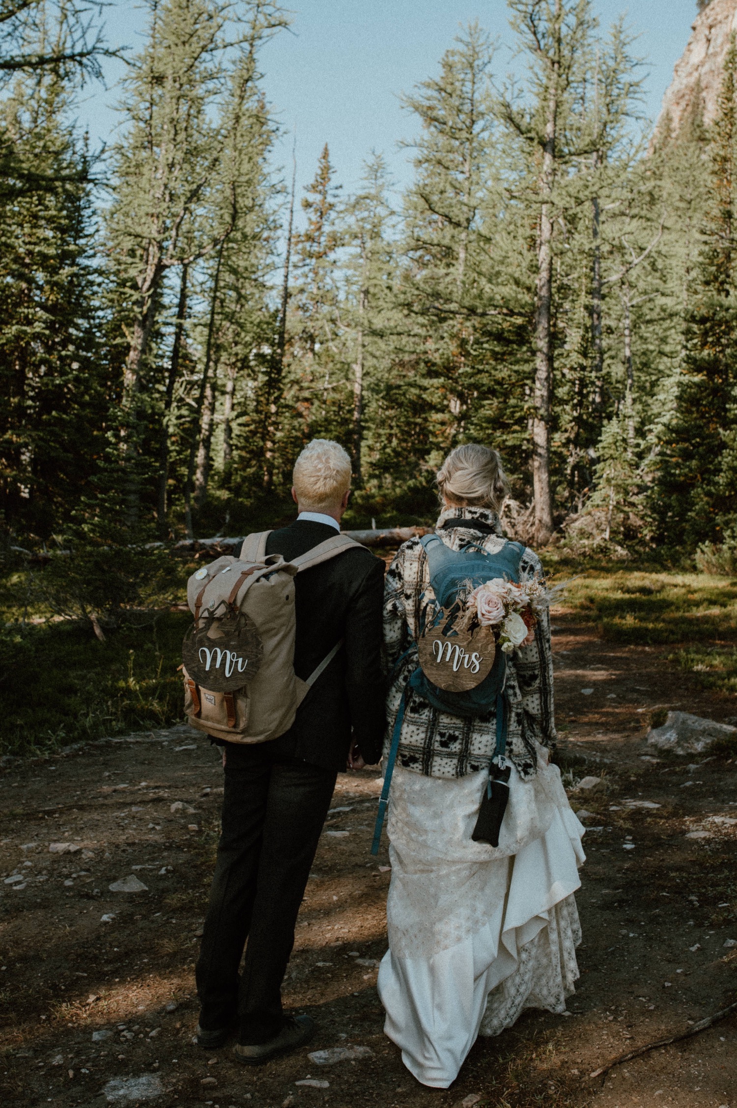 couple walking down forest trail with wooden Mr and Mrs signs for a styled hiking elopement in Lake Louise Alberta
