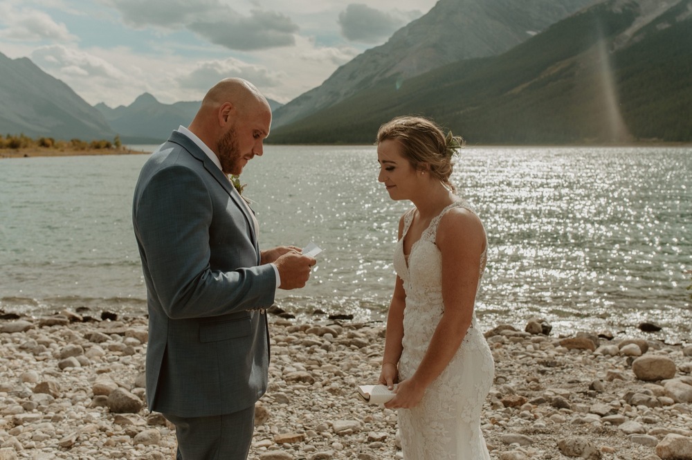 The bride and groom reading their vows at their Elopement ceremony on the shore of Spray Lakes in Kananaskis Alberta