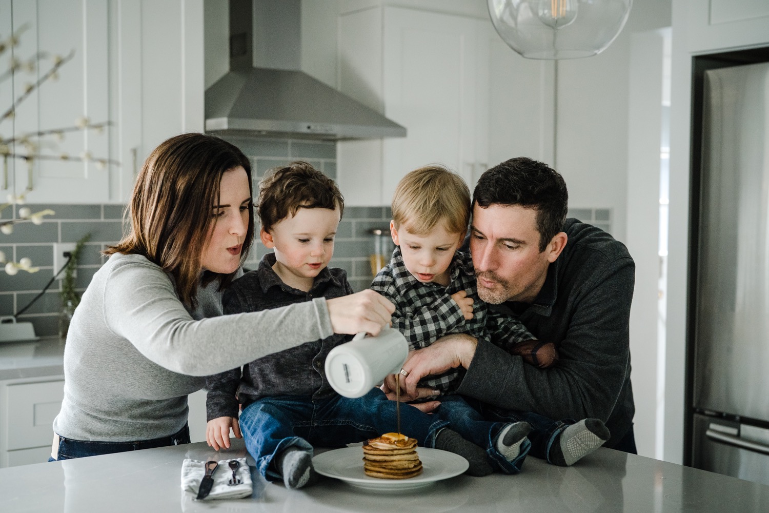 Family of 4 pouring syrup over plate of pancakes during in-home family session