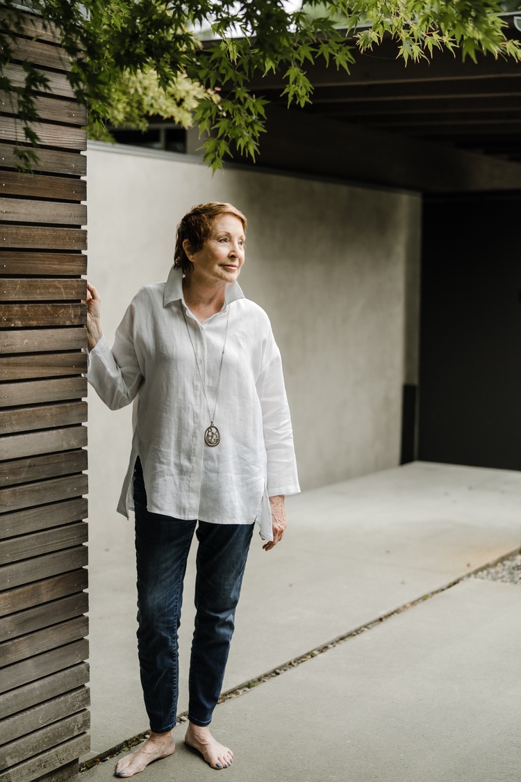 Woman leans against wood slat wall looking out into the distance