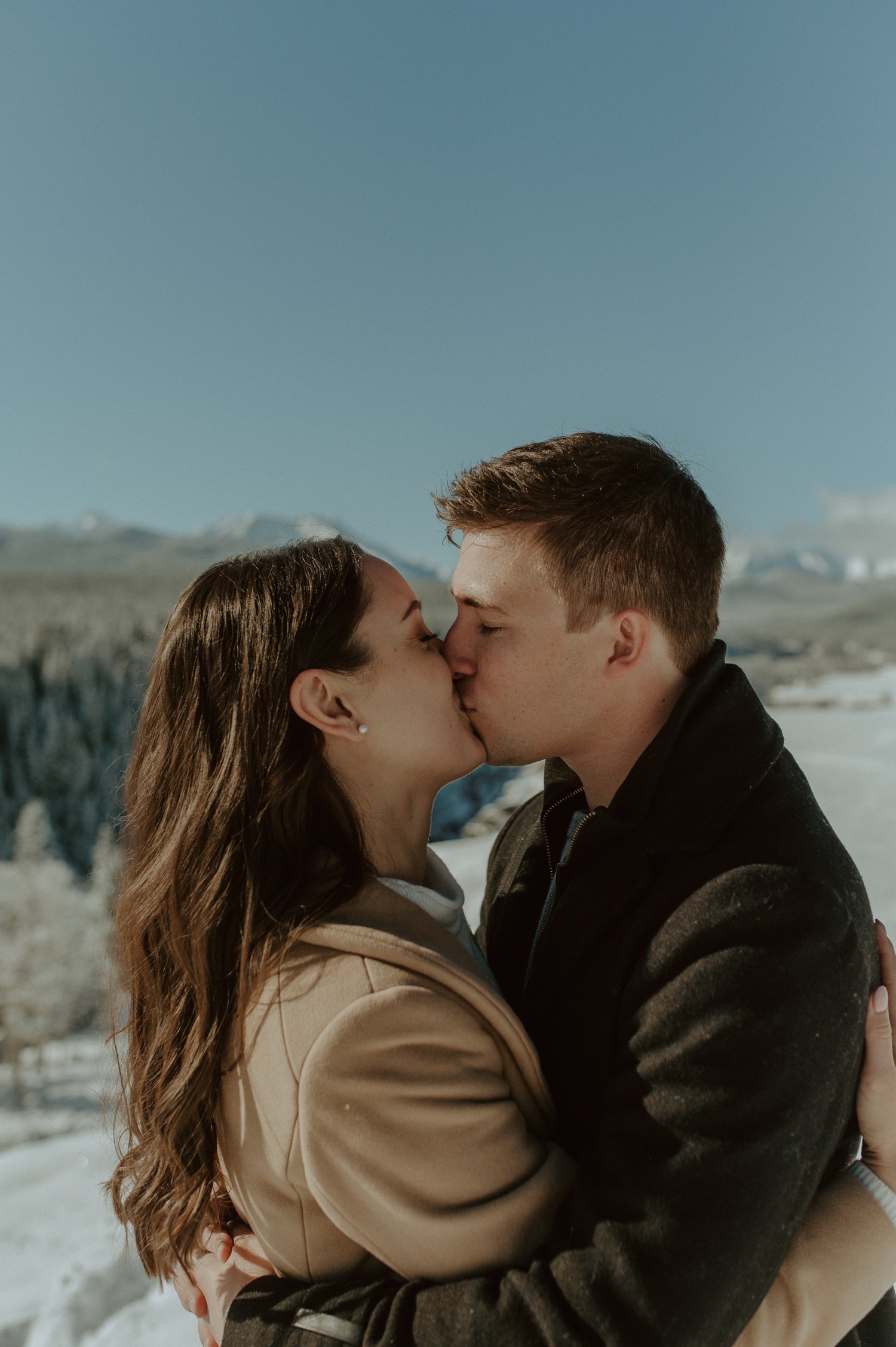 couple kissing in front of amazing back drop during a winter engagement session in the rocky mountains of Alberta