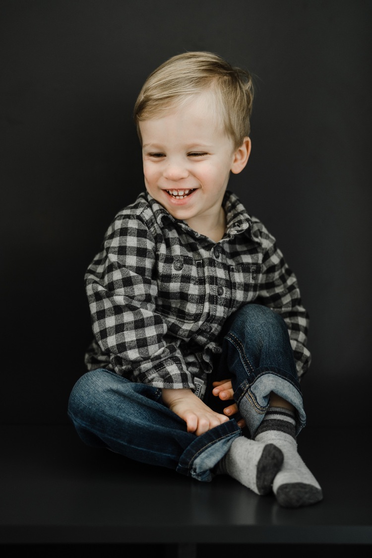 Little boy in plaid shirt sitting and smiling down at the ground