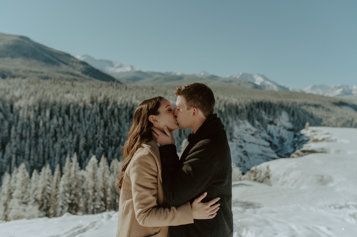 couple kissing in front of amazing back drop during a winter engagement session in the rocky mountains of Alberta