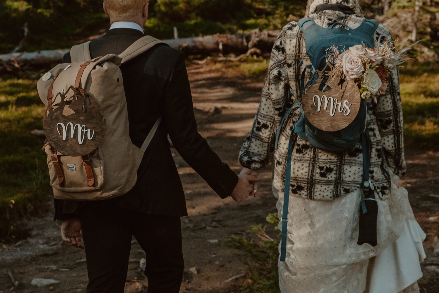 couple walking down forest trail with wooden Mr and Mrs signs for a styled hiking elopement in Lake Louise Alberta