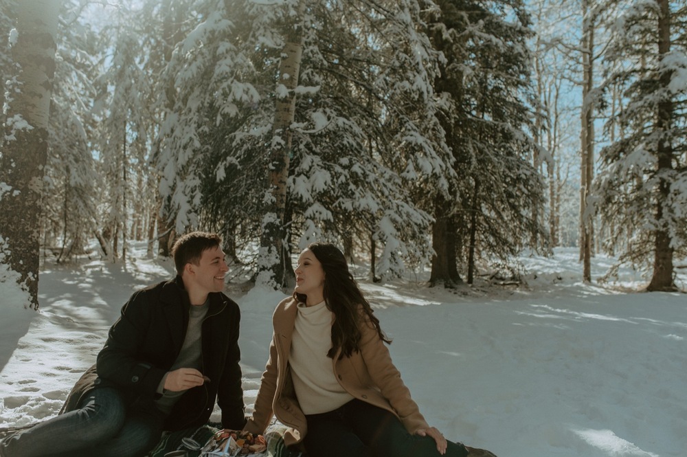 candid shot of couple enjoying a winter picnic during a winter engagement session in the rocky mountains of Alberta