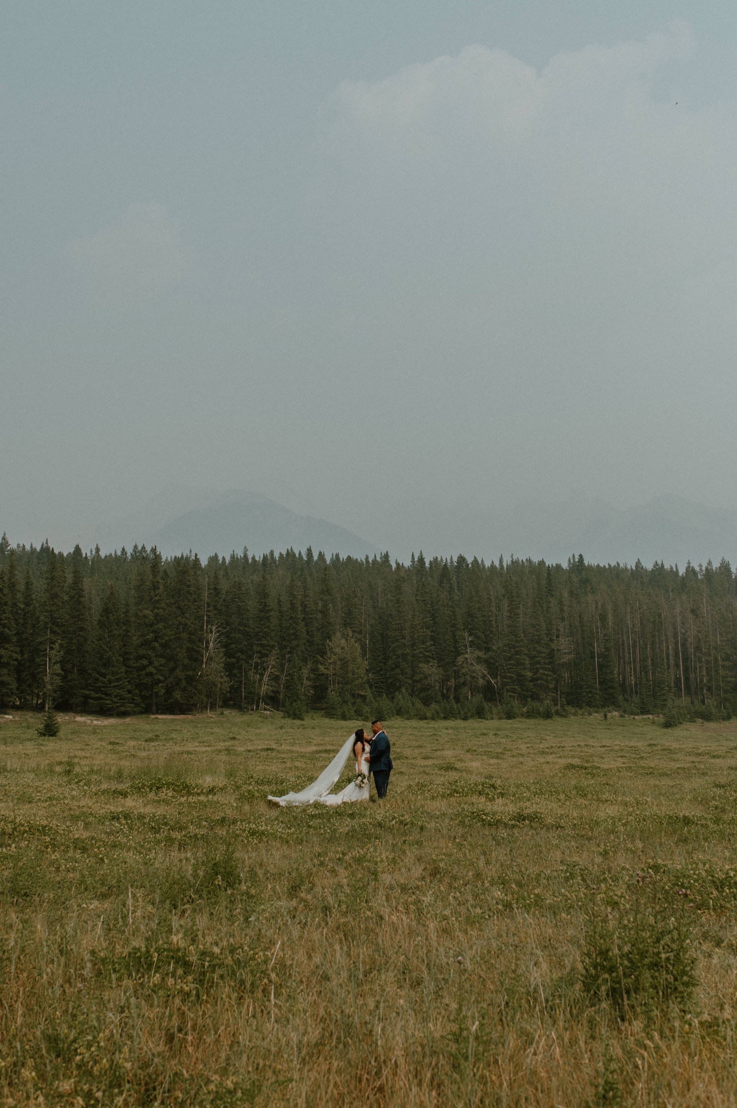 bride and groom in the distance posing for a mountain elopement during wildfire season in Banff Alberta