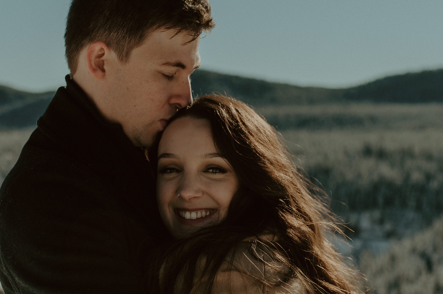 close up shot of couple cuddling and smiling in front of amazing mountain backdrop during a winter engagement session in the rocky mountains of Alberta