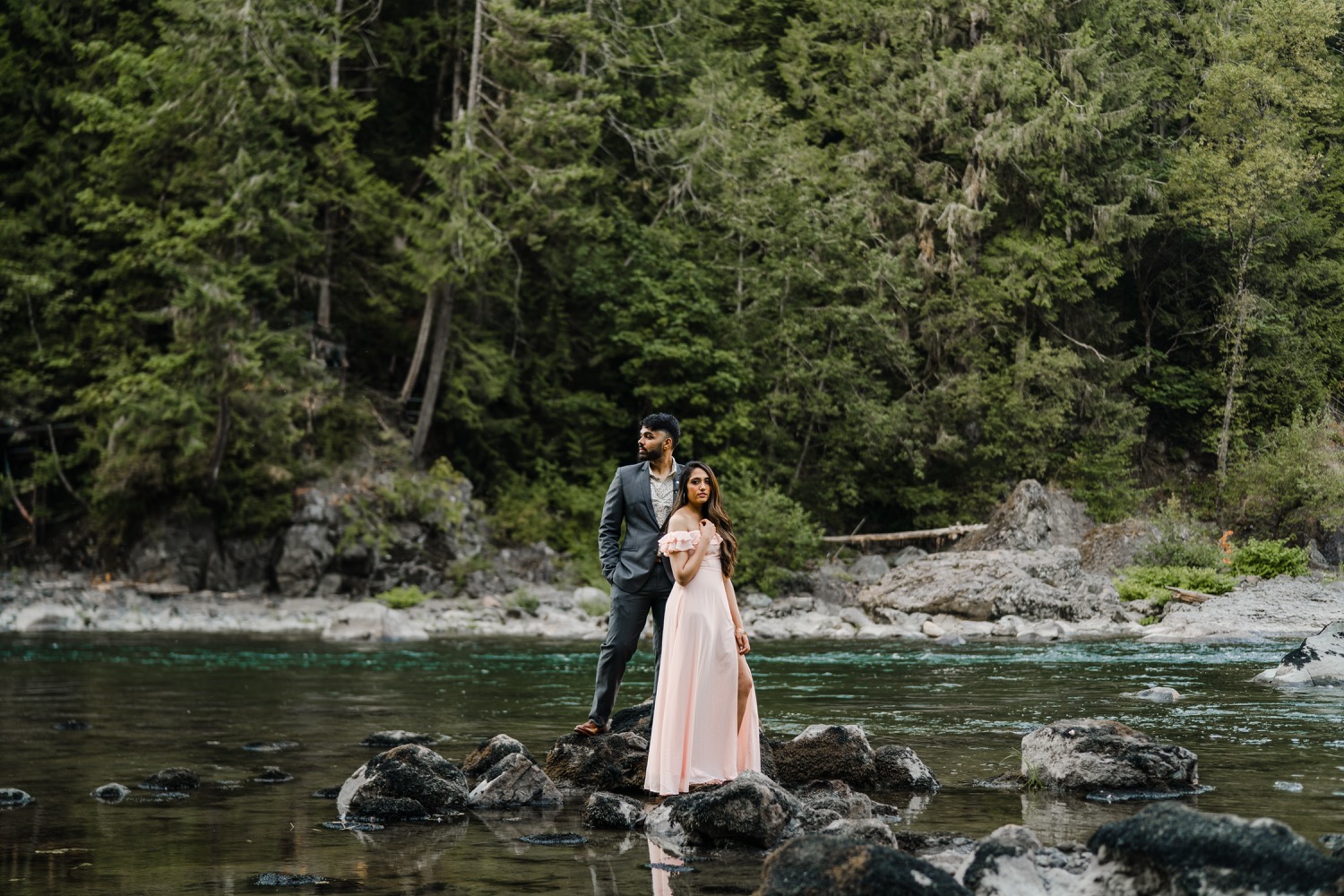 Couple standing on rocks in the river looking in opposite directions.