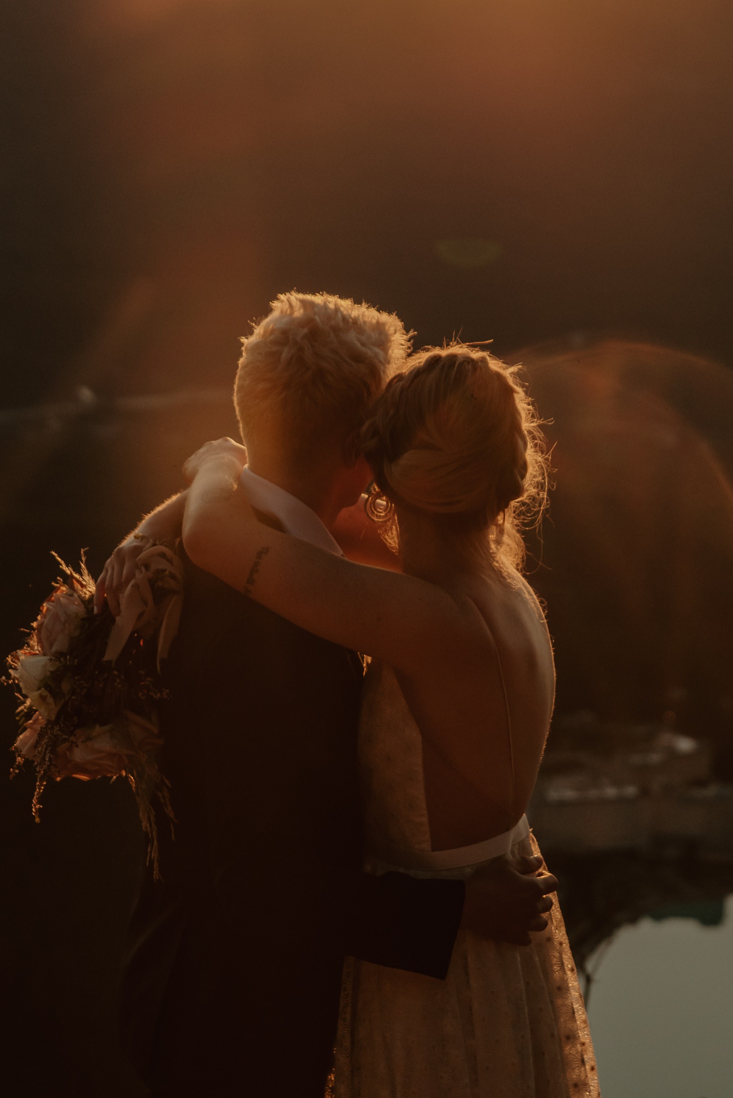 sun flare shot of couple embracing and kissing just as the sun rises above the mountain ridge during a hiking style elopement