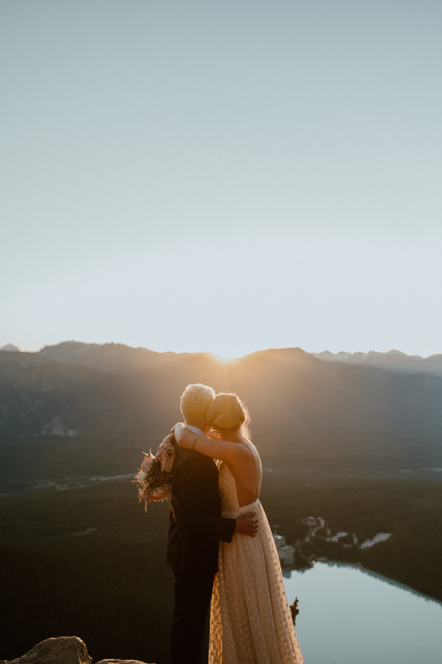 sun flare shot of couple embracing and kissing just as the sun rises above the mountain ridge during a hiking style elopement